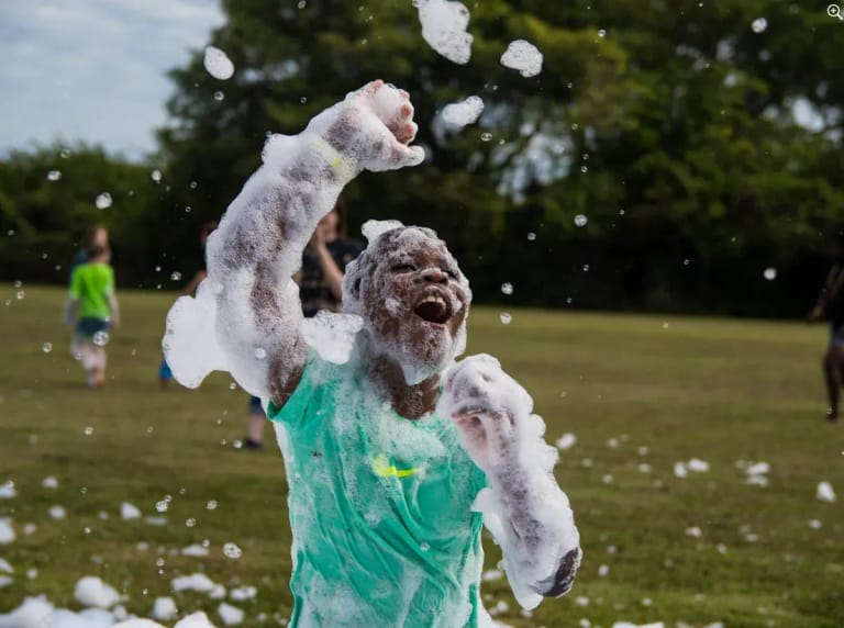 Joyful boy throwing foam in the air on a grass field at summer camp