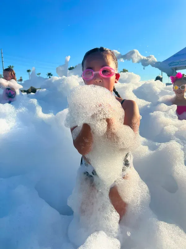 Girl wearing pink goggles holding a handful of foam at a birthday party